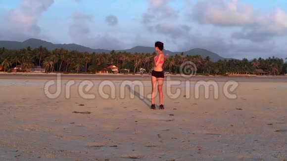 日落时分一位年轻女子在海滩上慢跑空中无人机射击慢动作视频的预览图