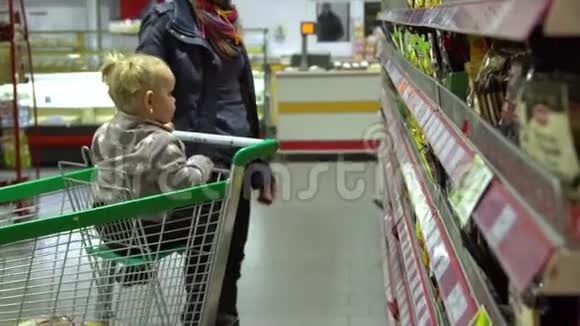 一个年轻的女人带着一个孩子在超市选择商品妈妈在手推车上驾驶一个小女孩妈妈和女儿视频的预览图