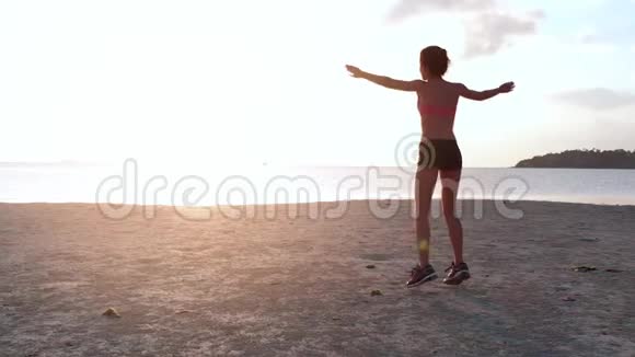 日落时分一位年轻女子在海滩上慢跑空中无人机射击慢动作视频的预览图