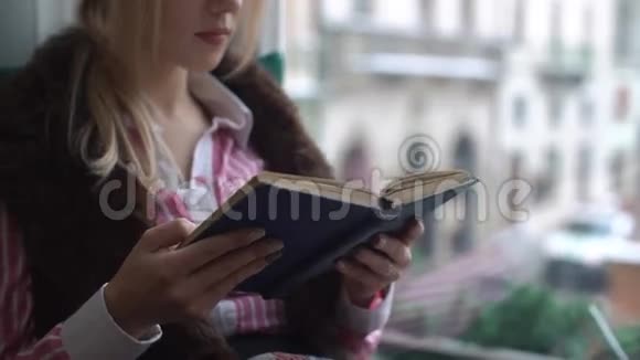 美丽的年轻女子坐在窗台上看书看着窗外视频的预览图