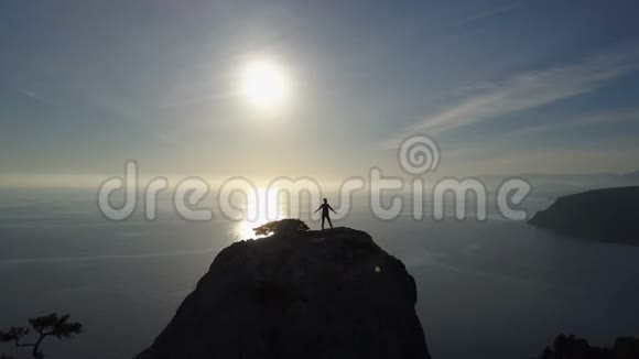 年轻女子站在山顶上面向大海的空中轮廓在美丽的山顶上的女士视频的预览图