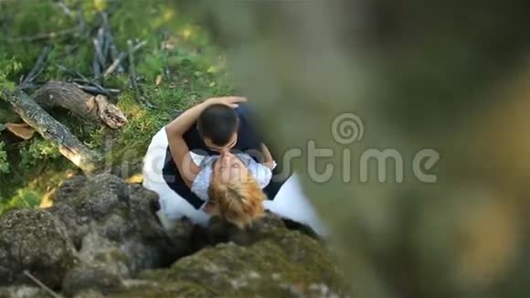 豪华快乐的金发新娘和时尚的新郎温柔地亲吻在绿色的夏日森林温柔的时刻顶部视图视频的预览图