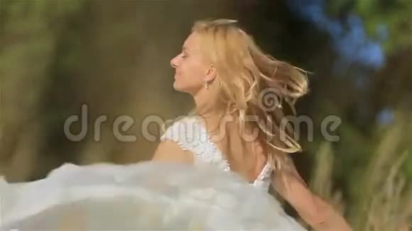阳光明媚的夏日迷人的金发年轻新娘在麦田里跳跃和微笑的肖像婚礼概念视频的预览图
