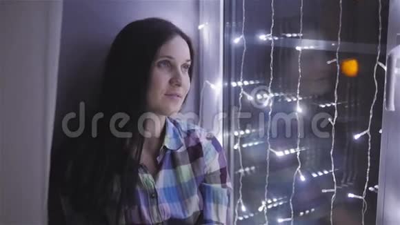 美丽迷人的女人坐在窗台上装饰着加兰新年圣诞节假日概念视频的预览图