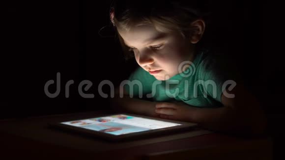 在黑暗中看平板电脑的小可爱女孩视频的预览图