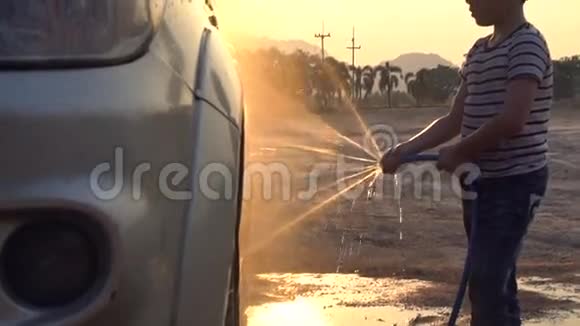 快乐的亚洲小孩用喷水冲洗汽车用日落和耀斑拍摄视频的预览图