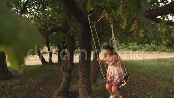 美丽的女孩喜欢在森林里的夏天晚上在秋千上飞行快乐的女孩在橡树上摇摆着绳子视频的预览图
