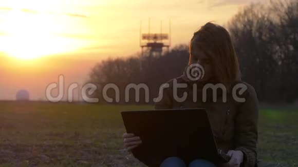 日落时分一个红发女孩在雷达附近使用笔记本电脑视频的预览图