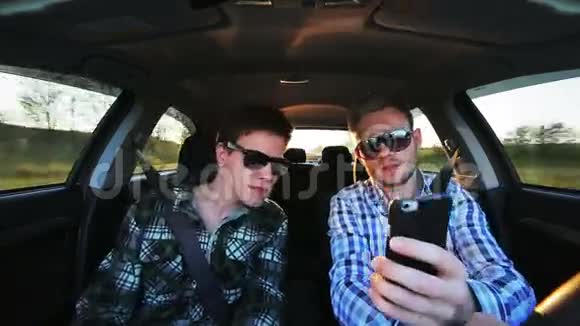 两个戴墨镜的男人开车在阳光明媚的日子里用电话视频的预览图