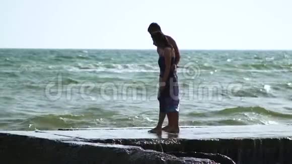 一对美丽的年轻夫妇在暴风雨中走在海边波浪在码头上破浪前进一个穿着泳裤的男人一个穿着泳裤的女孩视频的预览图