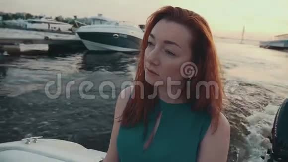 漂亮的红发女孩穿着绿松石的裙子在摩托艇上夏日之夜码头视频的预览图