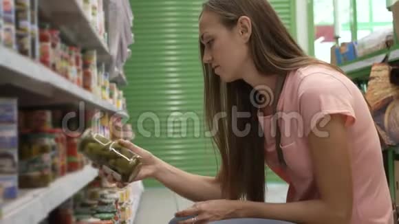 从超市货架上挑选罐头食品的女人读着标签视频的预览图