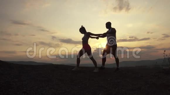 混合种族的剪影适合夫妇在户外锻炼在岩石山背景下日落体育健身视频的预览图