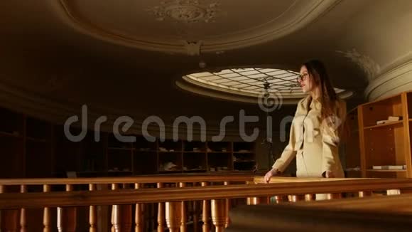 漂亮的金发女郎戴着眼镜在古老的老式图书馆里在温暖的苍白灯光下摆姿势视频的预览图