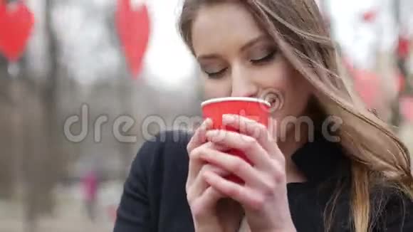 年轻美丽的金发女郎在秋天公园摆姿势装饰着红色的纸心背景饮酒杯视频的预览图