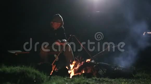 白种人坐在篝火旁晚上使用智能手机视频的预览图
