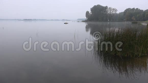 垂钓者坐在木船划艇上湖面覆盖着浓雾4K视频的预览图