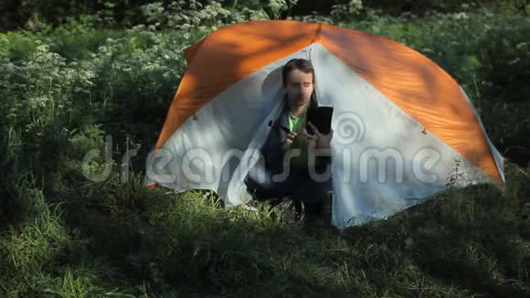一个男人坐在帐篷里在平板电脑上打视频电话早上在森林里视频的预览图