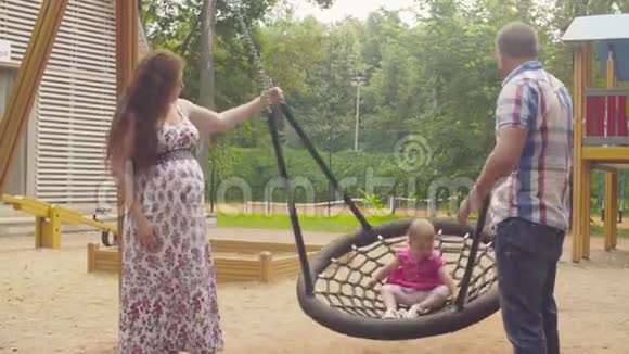 快乐的父母在秋千上摆动一个女婴视频的预览图