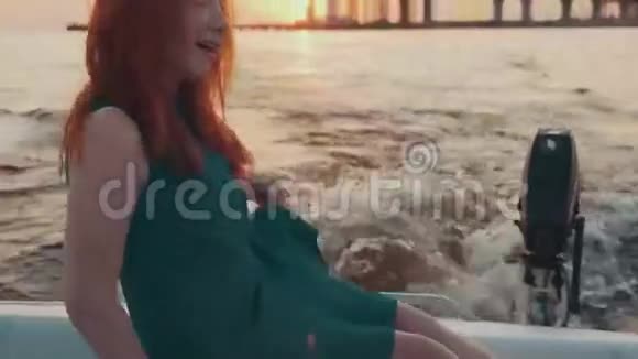 穿着绿松石衣服坐在摩托艇上的年轻女孩享受美丽的日落视频的预览图
