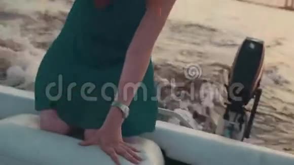 穿绿松石衣服的年轻女孩跪在摩托艇上日落很浪漫视频的预览图