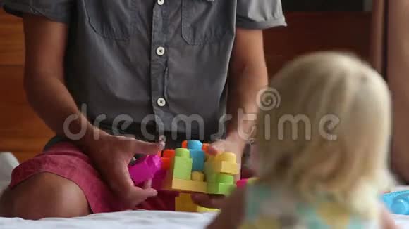 小女儿坐在爸爸的膝盖上在沙发上玩玩具书视频的预览图