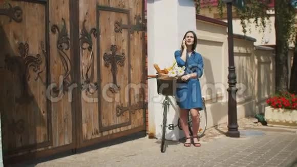 美丽的女孩站在街上骑着自行车篮子在电话里说话微笑着4K视频的预览图