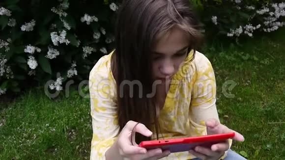 美丽的少年女孩带着平板电脑坐在公园的草地上静态相机的电影视频的预览图