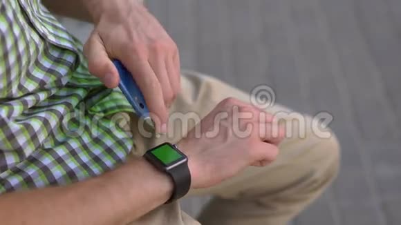 男人用他的小玩意智能手表智能手机坐在长凳上的绿色屏幕上视频的预览图