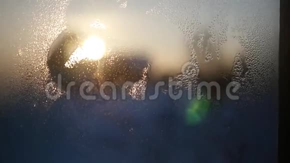 在美丽的日落和天空的背景下女性手在前景中擦拭玻璃上的水滴视频的预览图