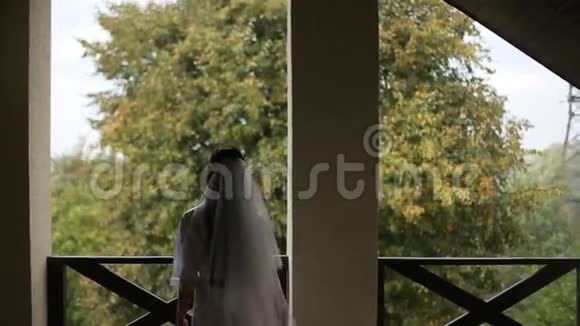 新娘戴着长长的婚纱站在露台上欣赏风景视频的预览图