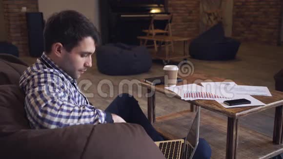 漂亮的男人穿着格子衬衫坐着休息看着显示器喝着咖啡视频的预览图