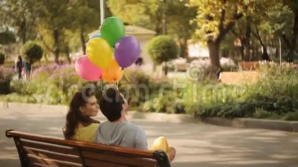 一对拿着气球坐在公园的长凳上视频的预览图