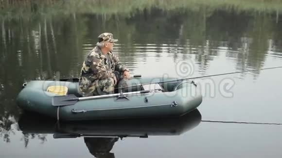 人摸着湖上的智能手表在充气船上拿着鱼竿的渔夫视频的预览图