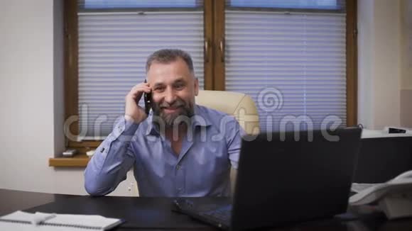 商人在一个很有趣的年龄与朋友在电话交谈在工作场所的办公室里视频的预览图