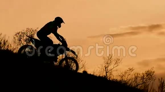 莫托科罗斯自行车在日落时滑下山摩托车手的剪影视频的预览图