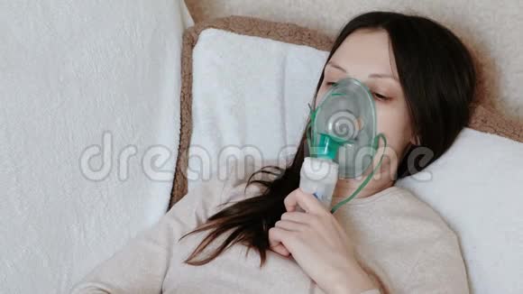 使用雾化器和吸入器进行治疗躺在沙发上的年轻女人通过吸入面罩吸入侧视视频的预览图
