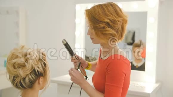 豪华美容院的女理发师正在与年轻的金发模特站在一起工作视频的预览图