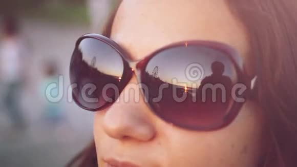 这位年轻的黑发女人透过眼镜看着太阳在夕阳的天空下1920x1080视频的预览图