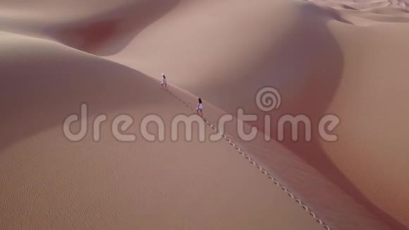 两个女人在日出时走在沙丘上从无人机上看视频的预览图