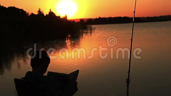 一个男孩正在看一本书书上写着日出时的钓鱼日落时太阳在水面上刺眼视频的预览图