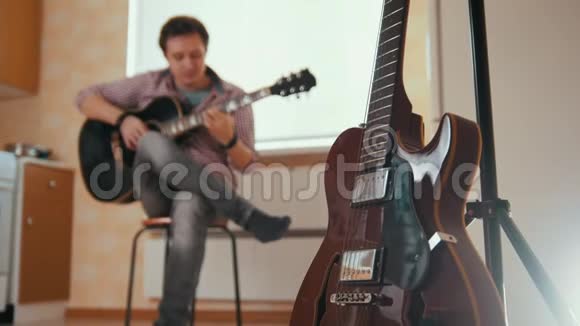 年轻有魅力的男人用吉他和戏剧作曲前景中的其他乐器模糊了视频的预览图