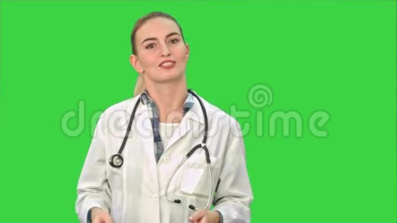 微笑着穿着实验室外套的漂亮女人在绿色屏幕上与相机交谈Chroma键视频的预览图