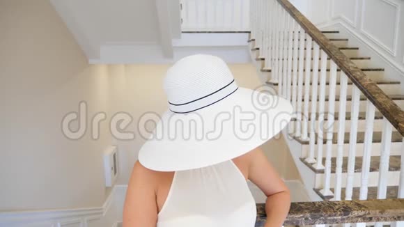 一个戴着白色大帽子的女人走下一个白色的大楼梯4k慢动作视频的预览图