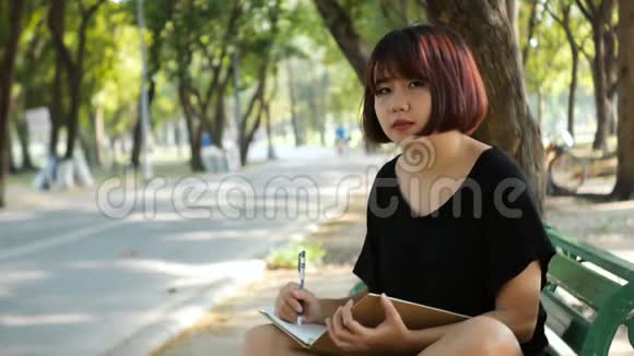 快乐时髦的年轻亚洲女人在公园写日记快乐时髦的年轻亚洲女人在公园做笔记本视频的预览图