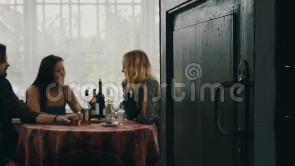 两个女孩和男人在桌子上说话在乡间别墅的露台上喝酒视频的预览图