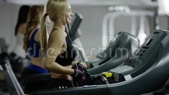 带着白色耳机在跑步机上行走的年轻女子视频的预览图