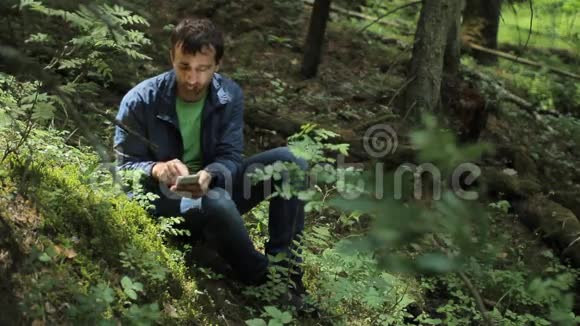 森林里的人在电话里拍照它坐在绿色的小悬崖上视频的预览图