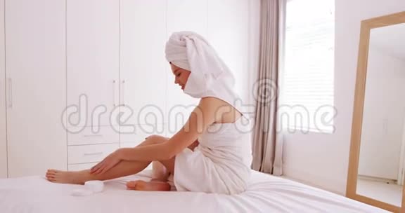 在卧室的腿上涂润肤霜的女人视频的预览图