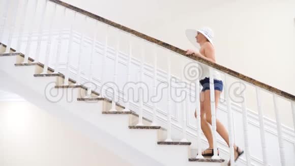 一个戴着白色大帽子的女人走下一个白色的大楼梯4k慢动作视频的预览图